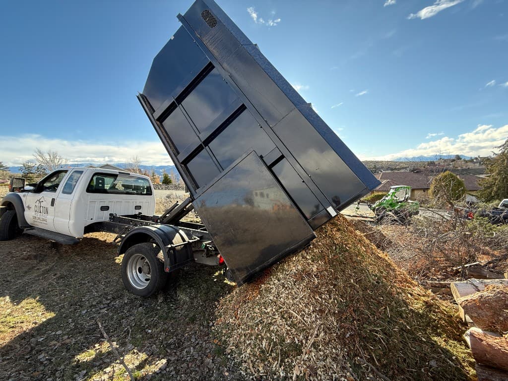 Chip truck with raised dump box unloading a full load of fresh wood chips at a drop site